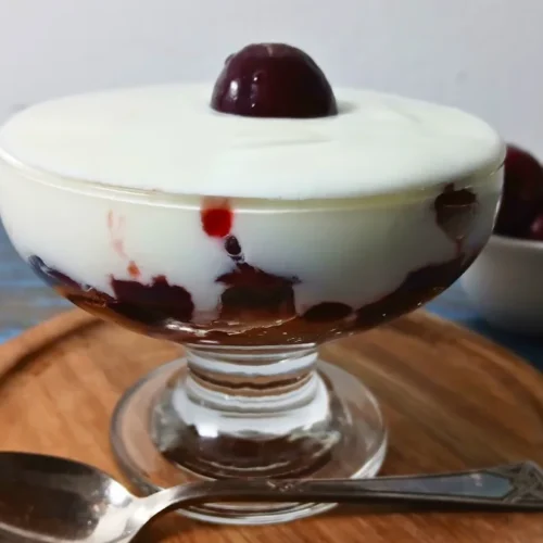 Single-serving cherry yoghurt trifle layered with leftover cake, cherry jam, fresh cherries, and creamy yoghurt in a glass dessert bowl, topped with a whole cherry.