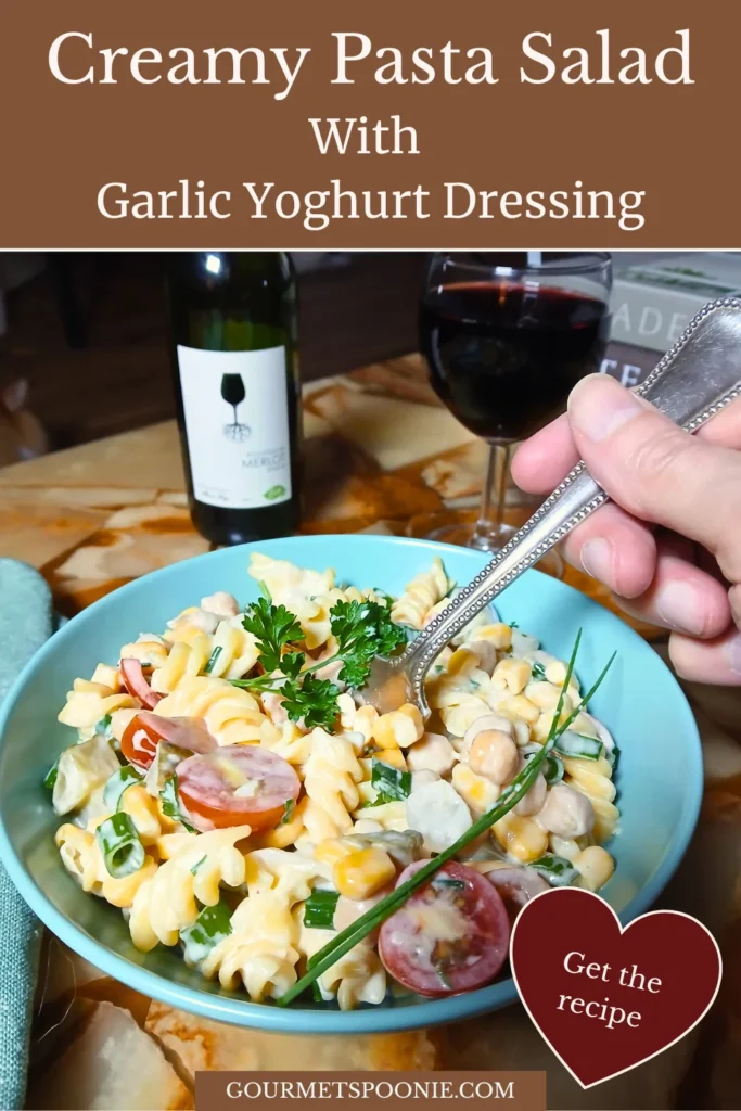 Fork lifting a bite of creamy gluten-free pasta salad with cherry tomatoes, beans, sweetcorn, herbs, and garlic yoghurt dressing.